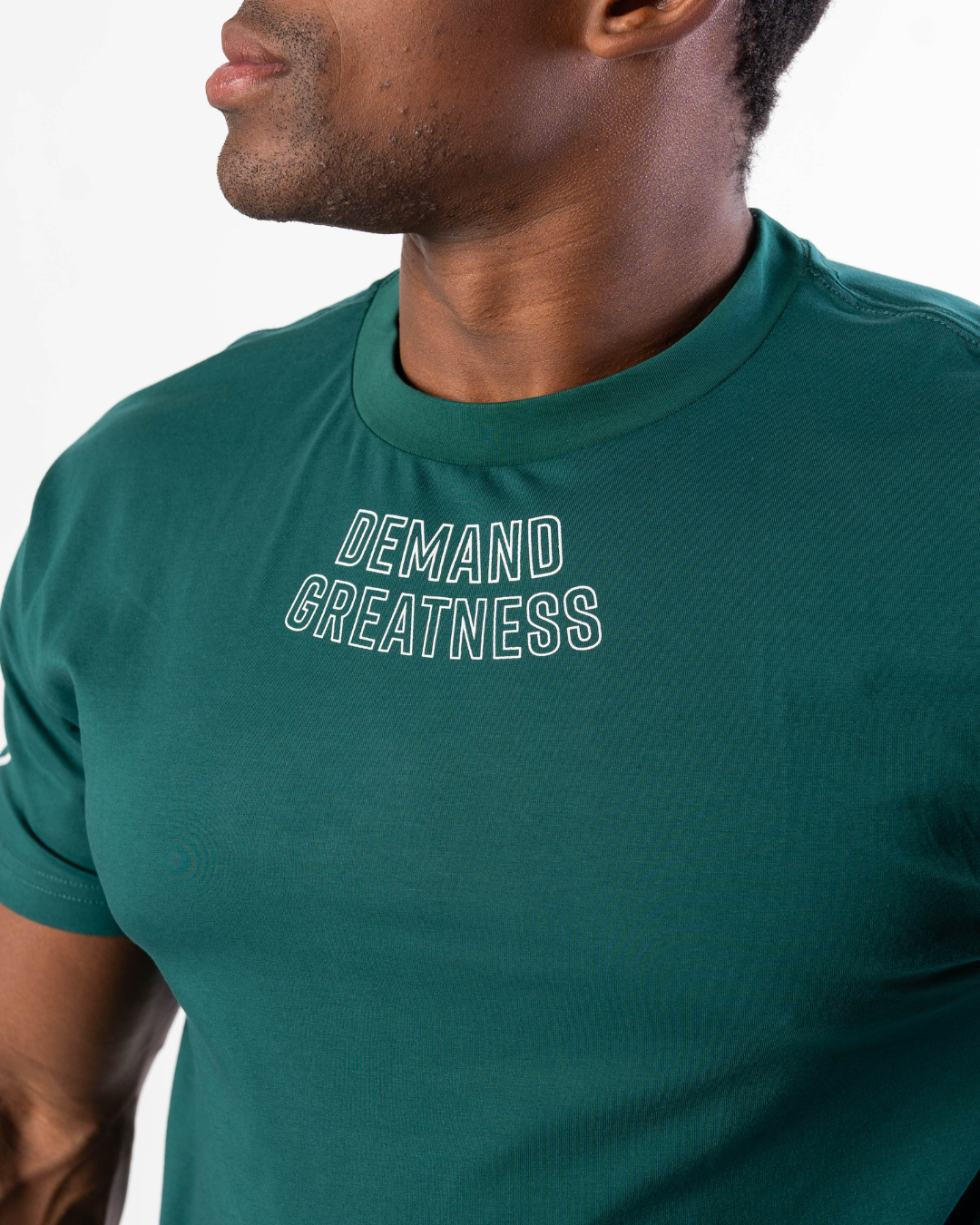 Close-up of “Demand Greatness” chest print on the Emerald Forás True‑Fit Meet Shirt, with bold white typography contrasting against rich green stretch fabric.