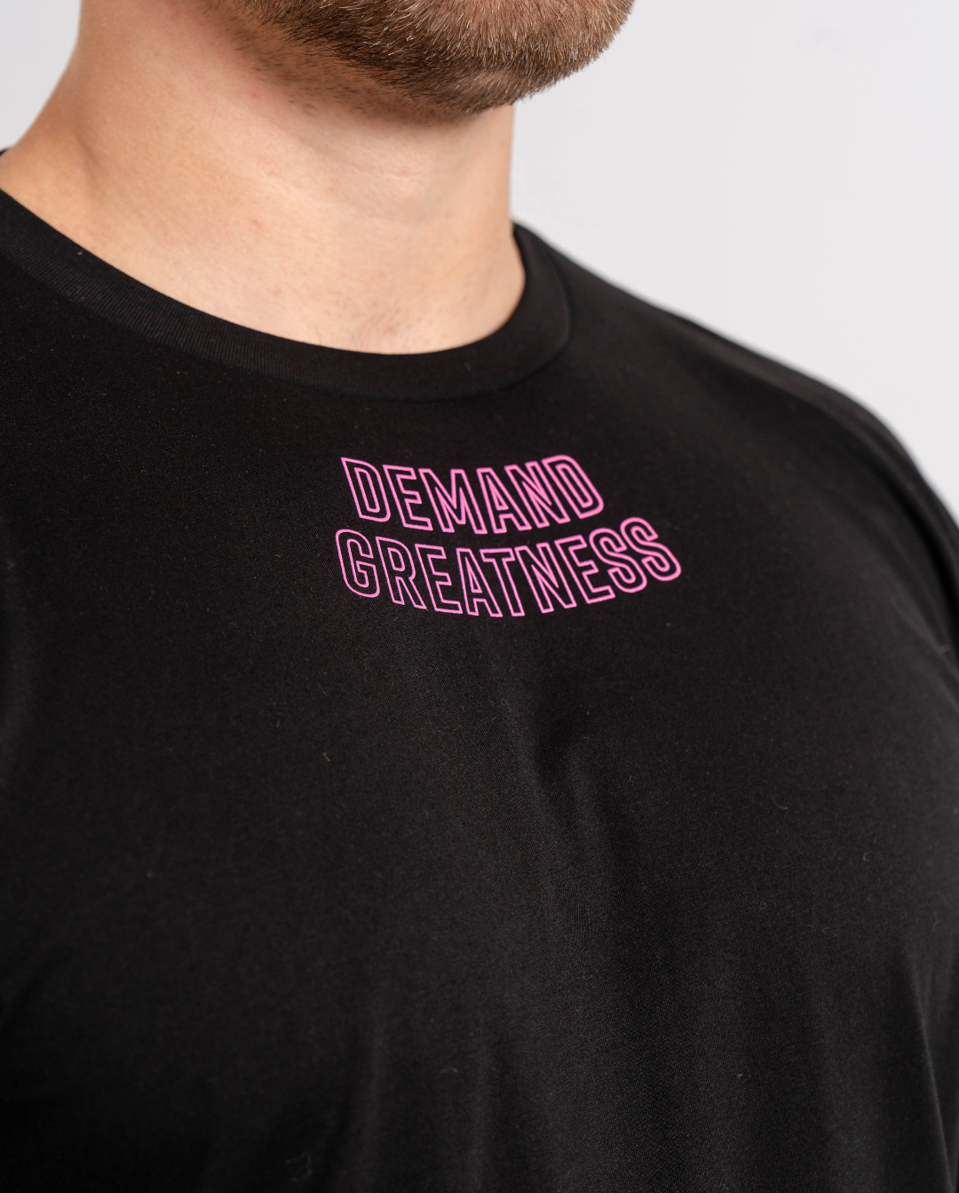 Close-up of “Demand Greatness” printed across the chest of the Flamingo True‑Fit Meet Shirt, with bold white text standing out on vibrant pink fabric.