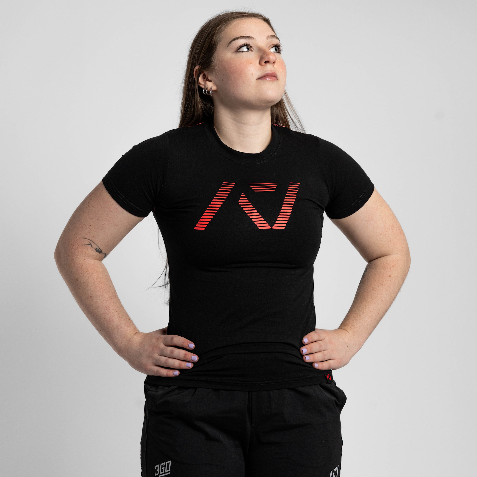 Person wearing a black t-shirt with a logo and black shorts on a light gray background