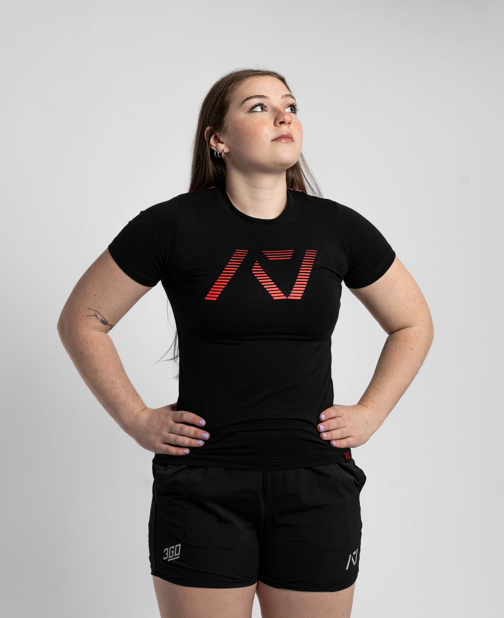 Person wearing a black t-shirt with a logo and black shorts on a light gray background