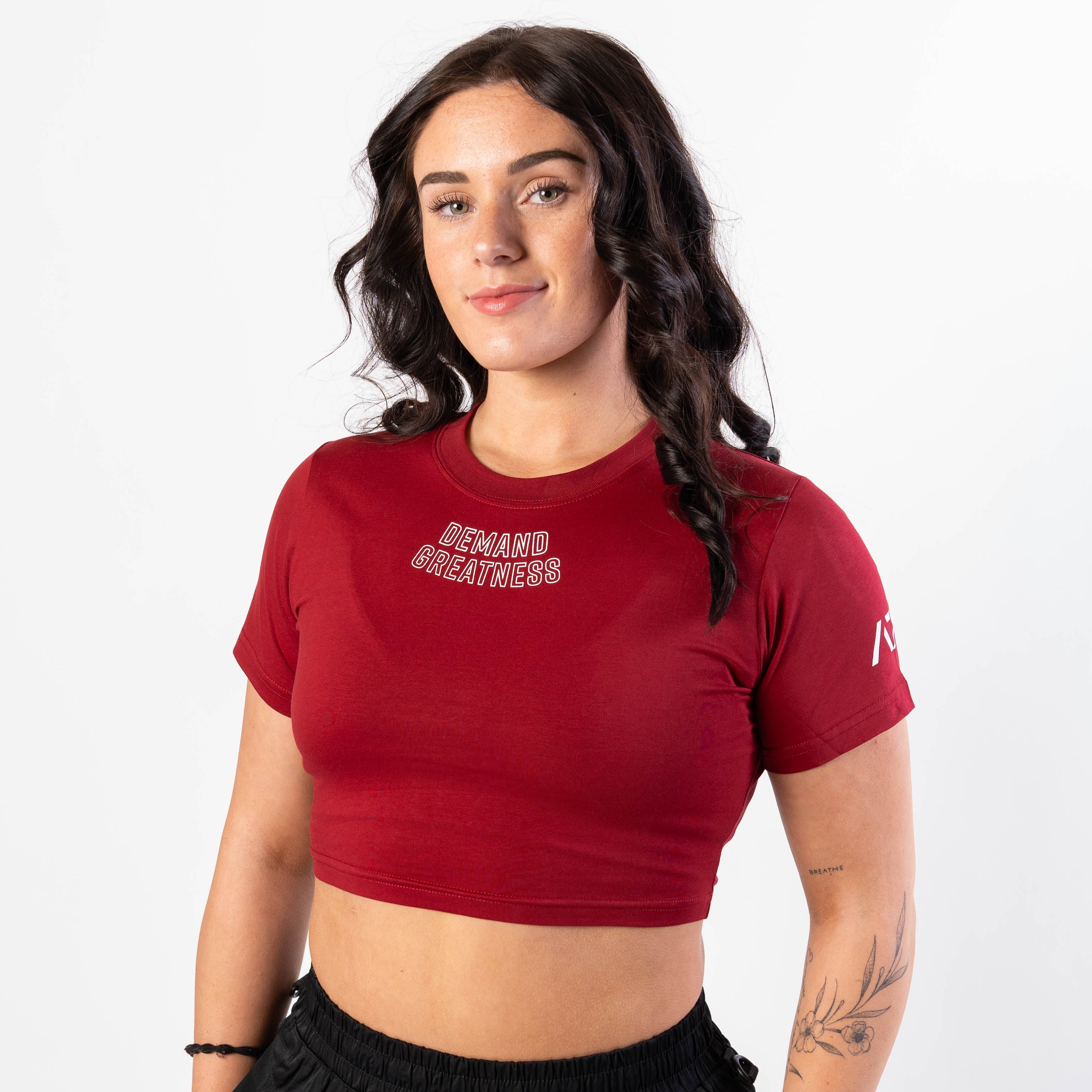 A woman wearing a red meet crop with 'Demand Greatness' text on the upper chest and the A7 logo on the upper back and sleeves.