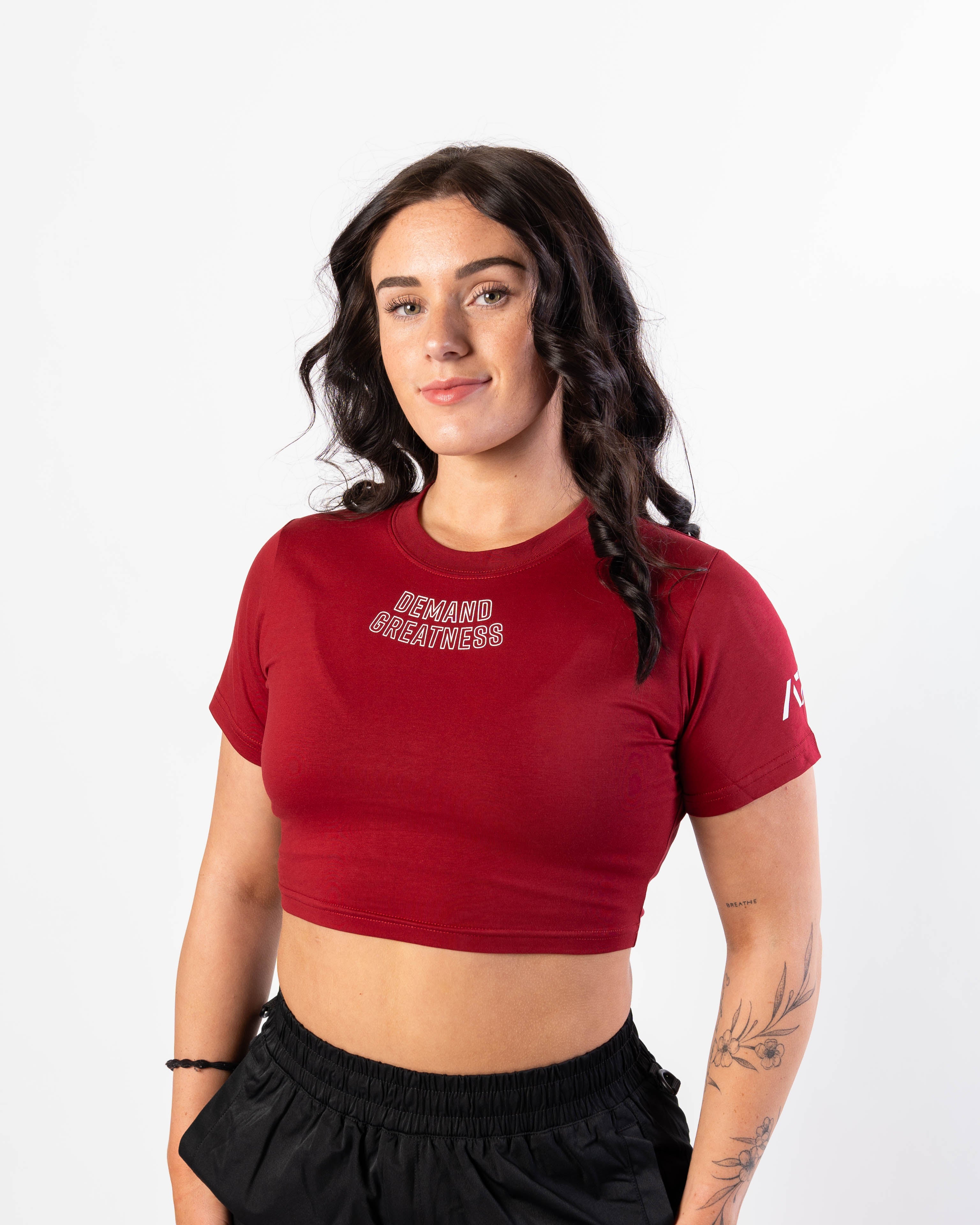 A woman wearing a red meet crop with 'Demand Greatness' text on the upper chest and the A7 logo on the upper back and sleeves.