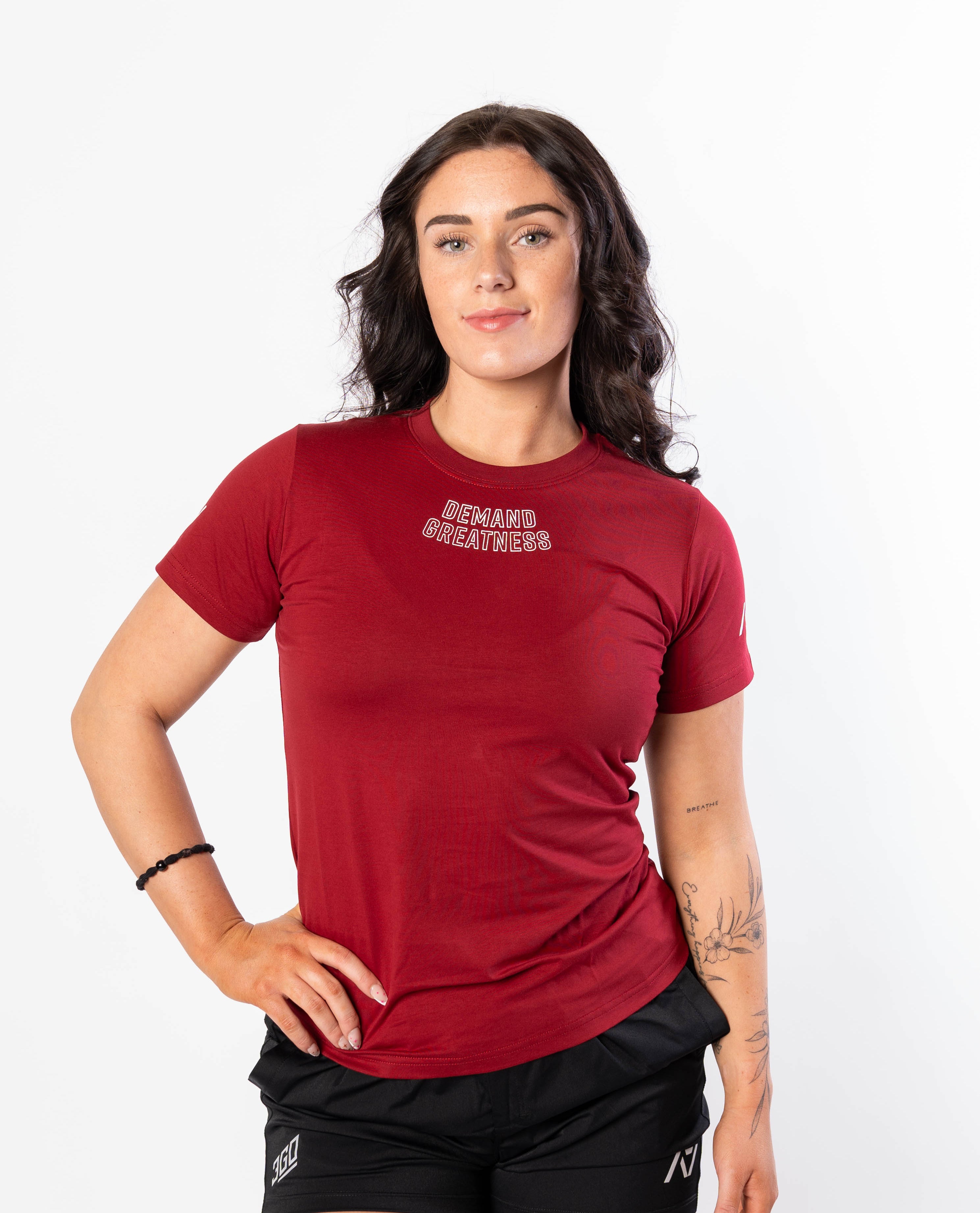 A woman wearing a red Demand Greatness True-Fit women's meet shirt with a logo on the upper chest and upper back.