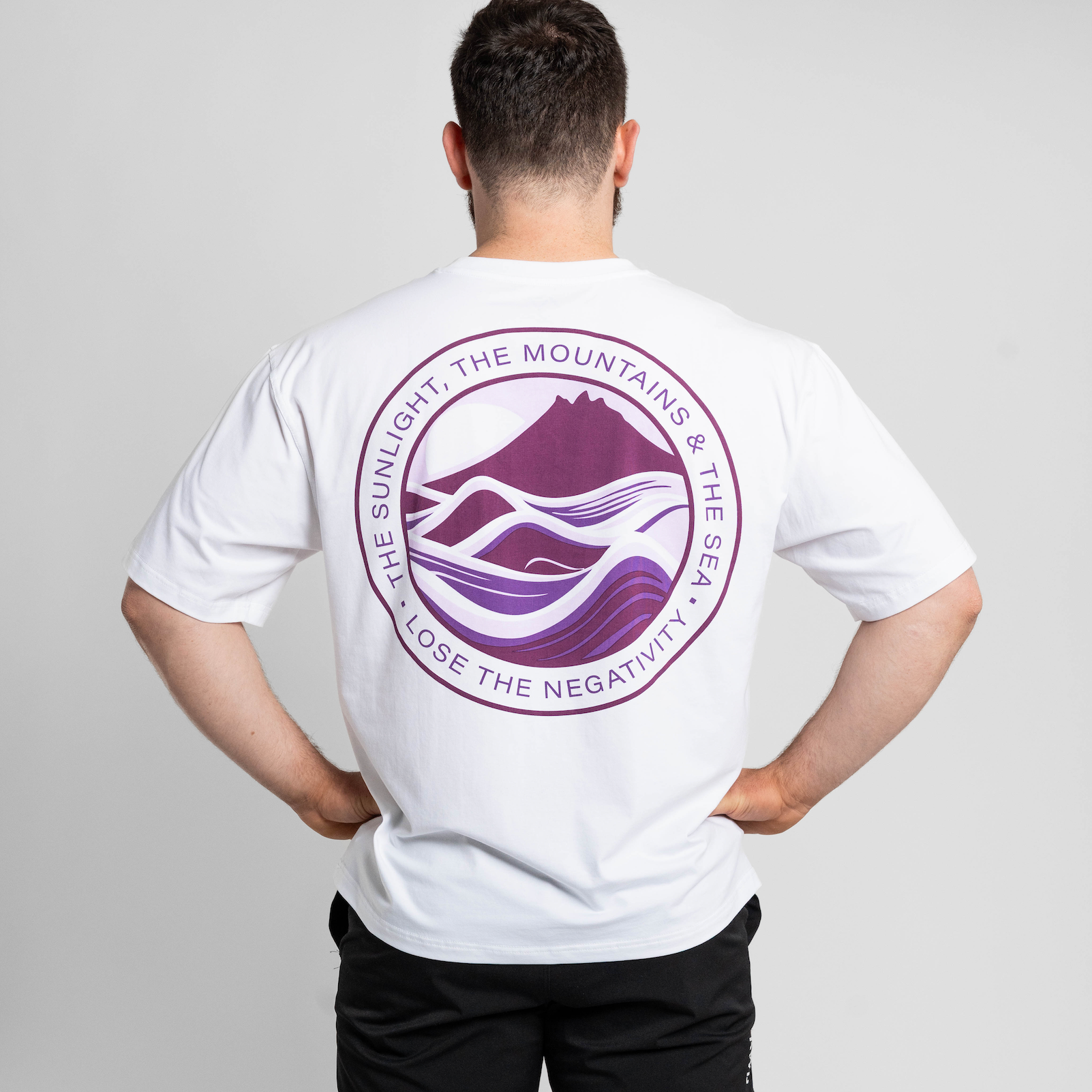 Person wearing a white t-shirt with a purple logo on the back, standing against a plain background