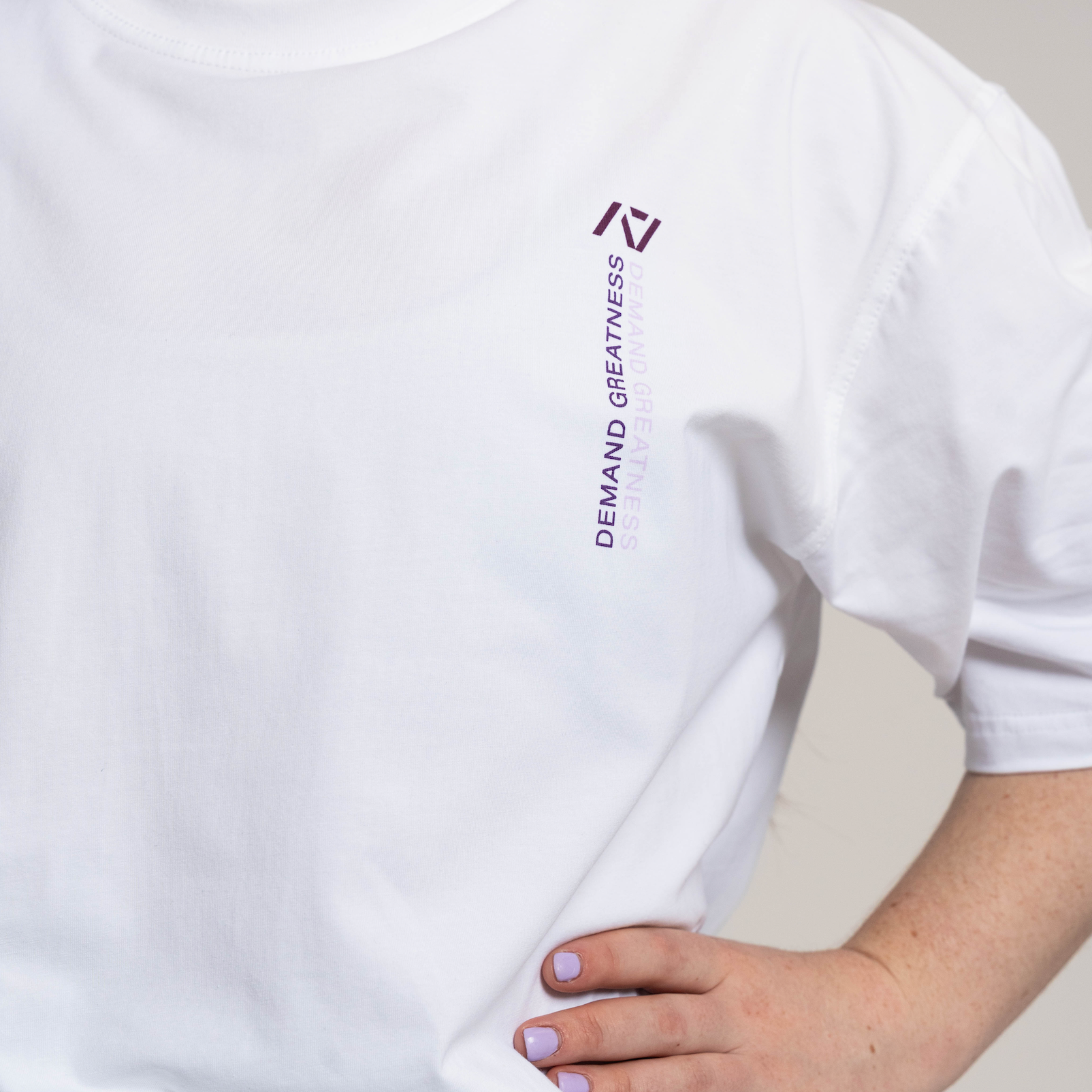 White oversized t-shirt with a logo and text worn by a person, on a neutral background