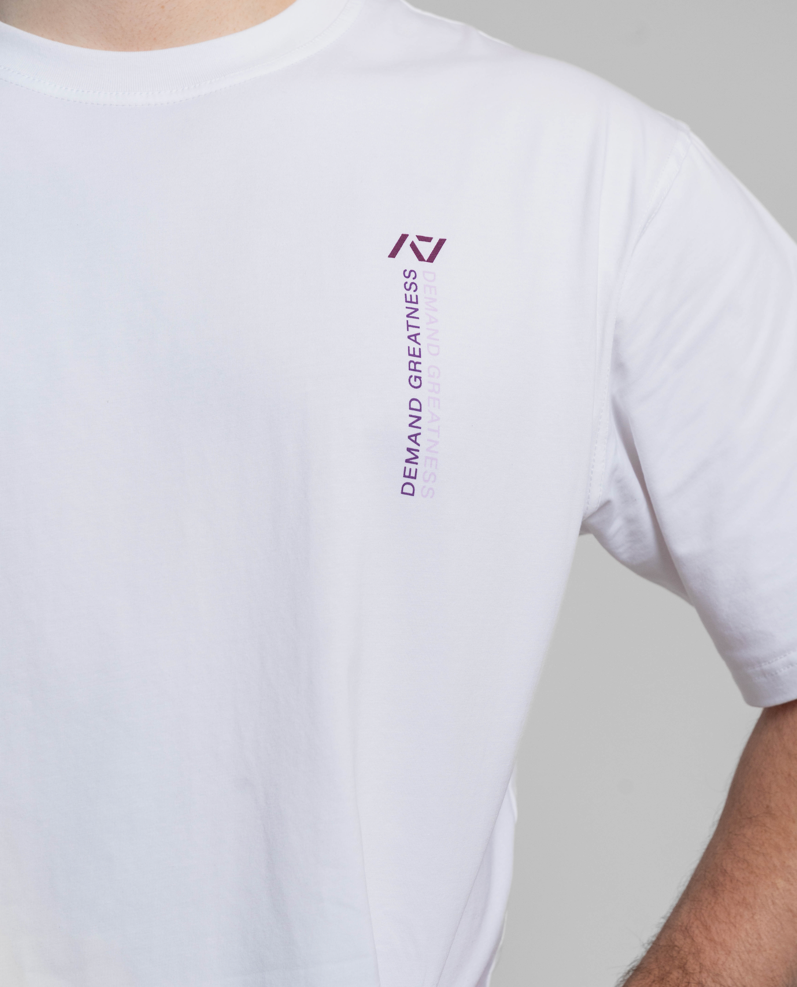 White t-shirt with a logo and text on the sleeve against a gray background