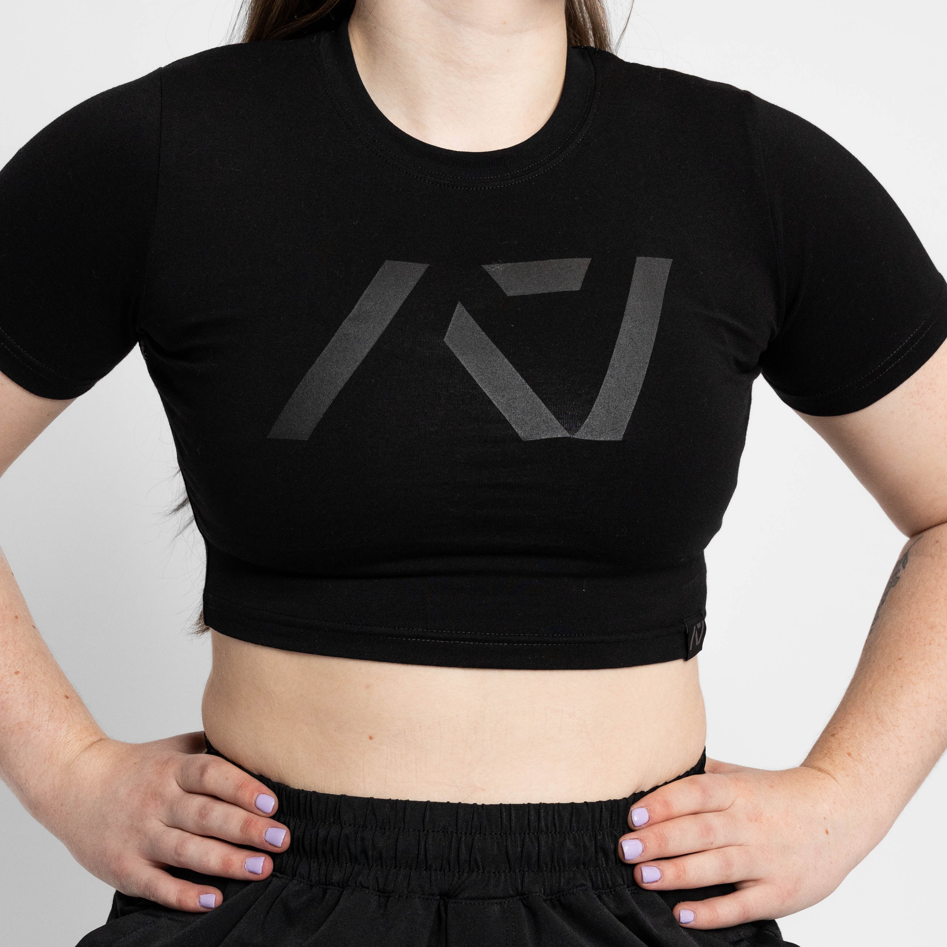 Person wearing a black crop top with a logo on a plain background