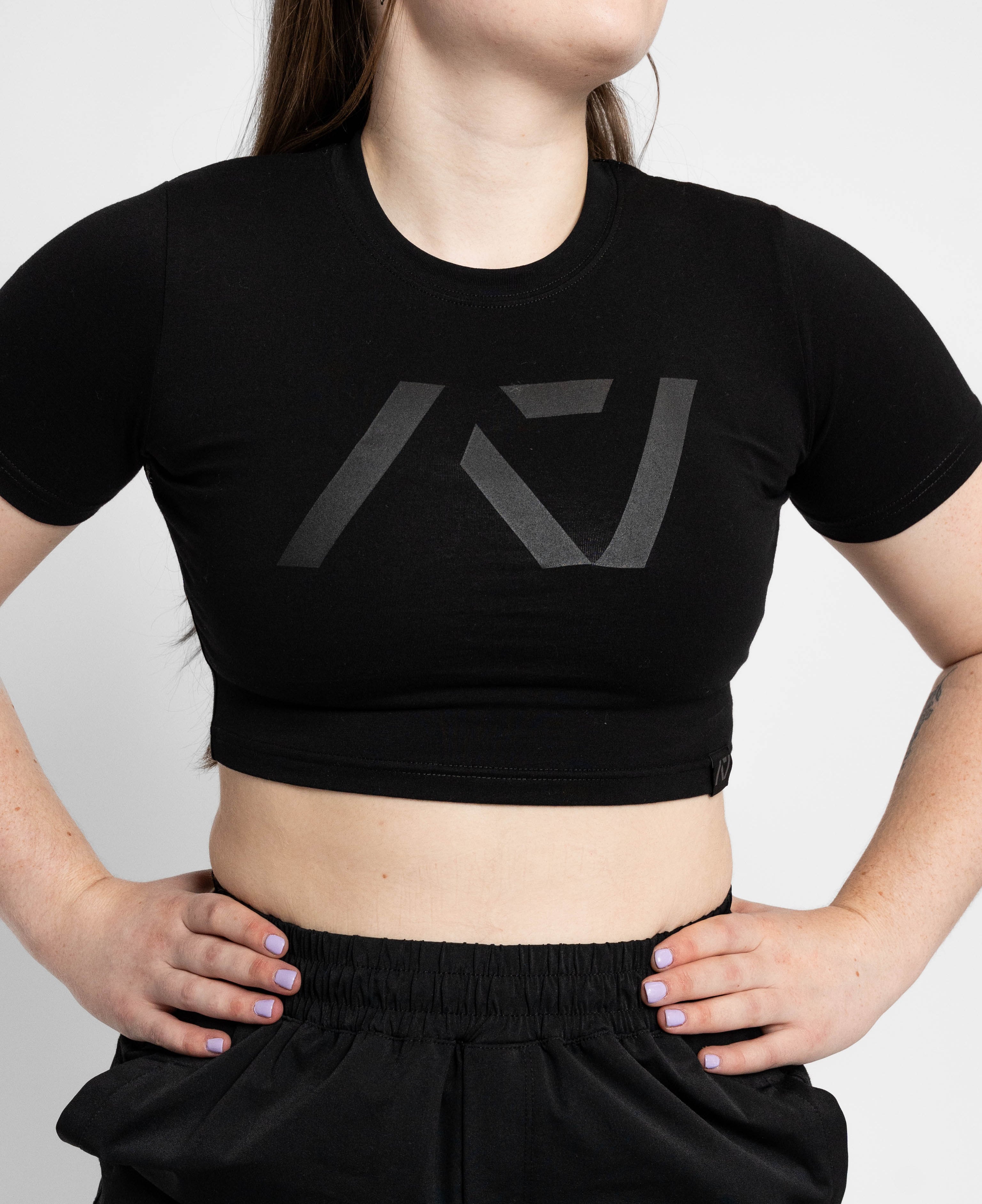 Person wearing a black crop top with a logo on a plain background