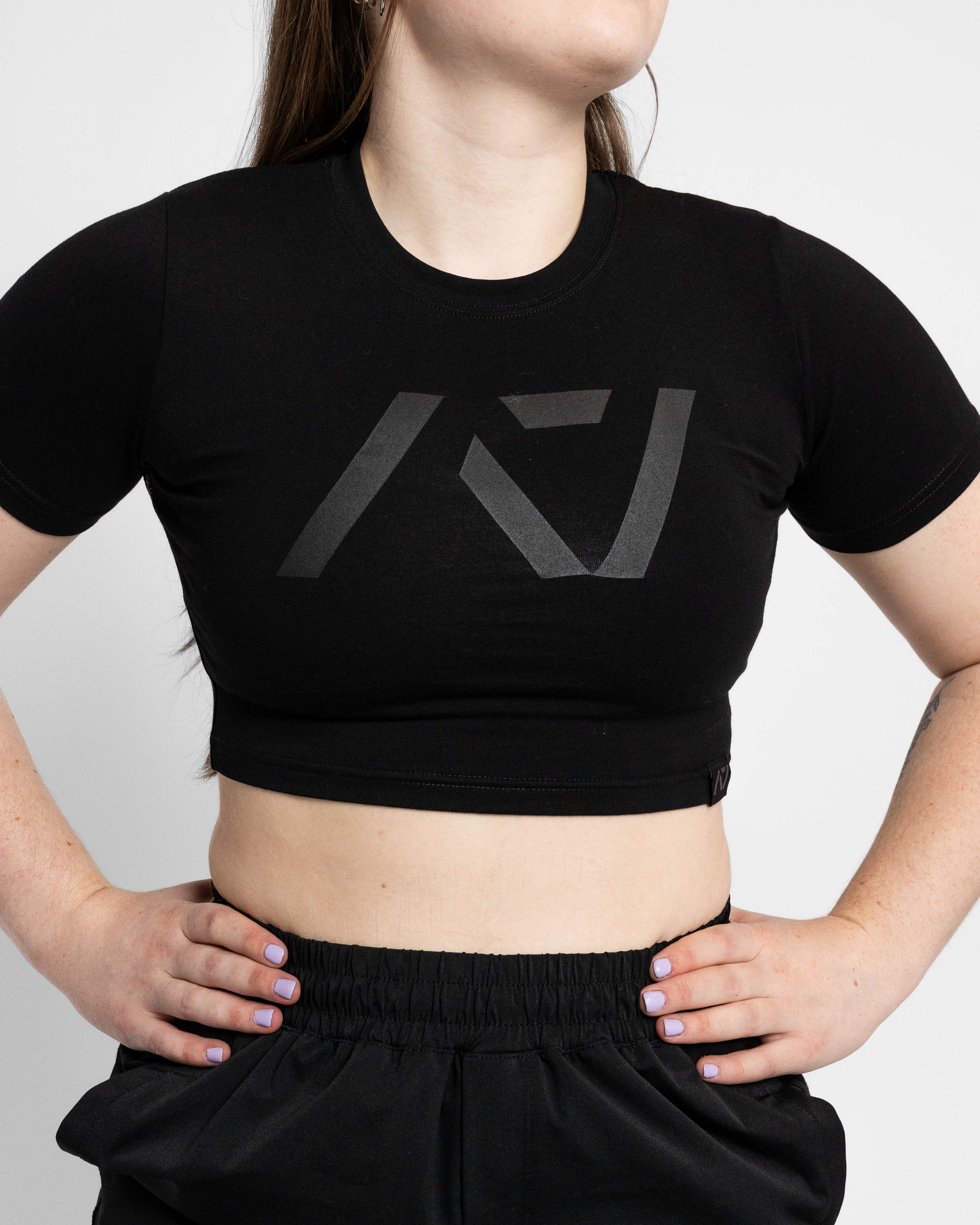 Person wearing a black crop top with a logo on a plain background