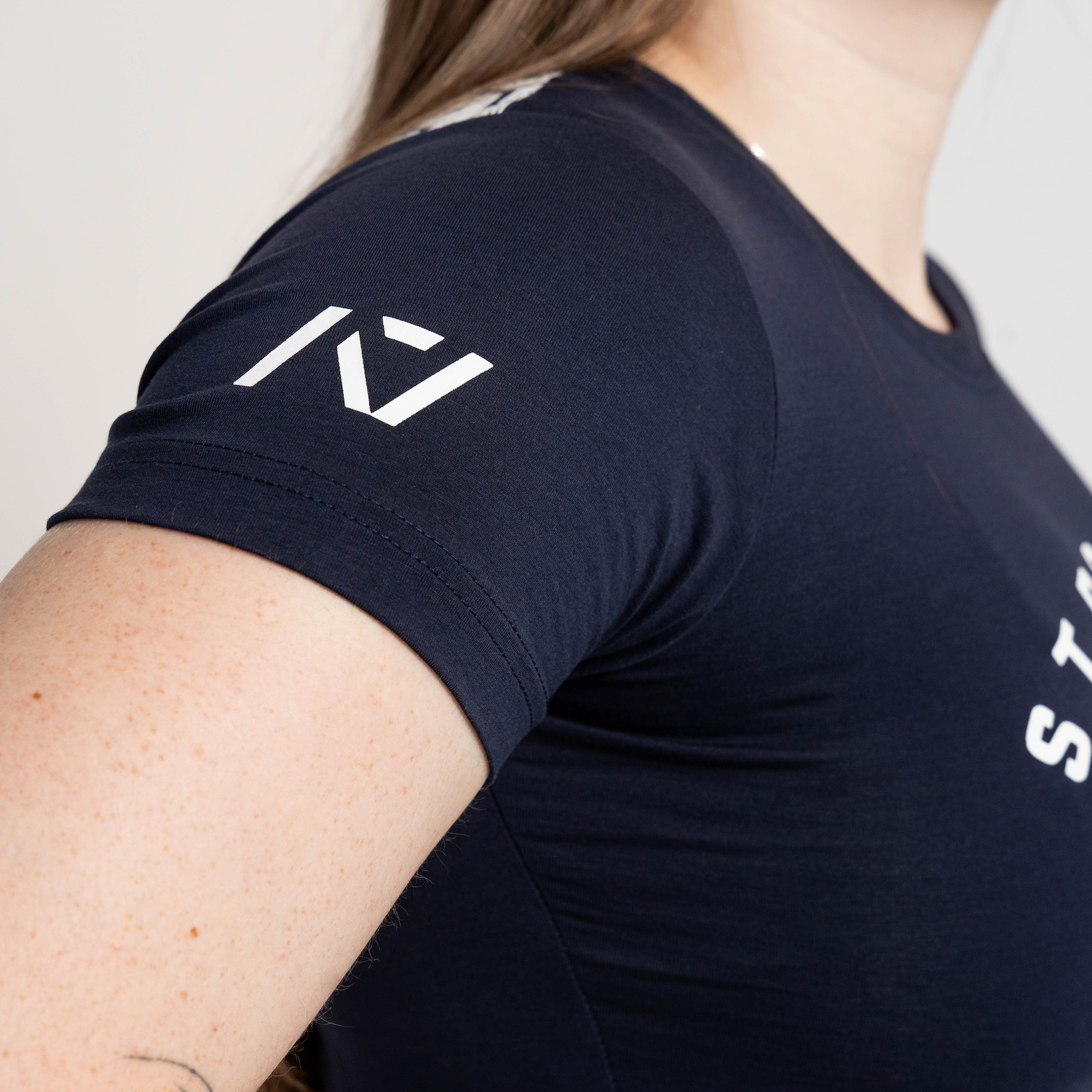 Person wearing a black t-shirt with a logo on the sleeve against a neutral background