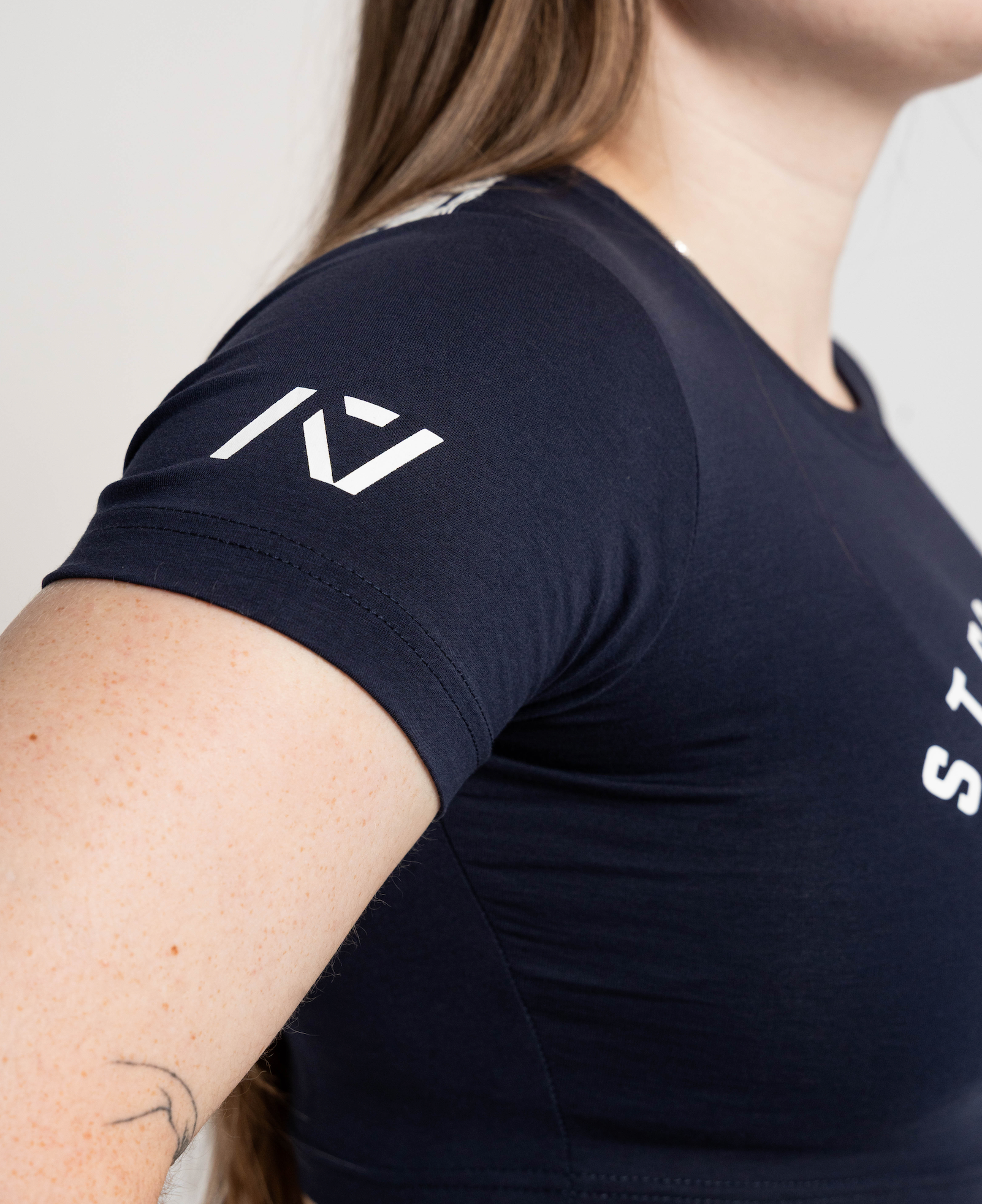 Person wearing a black t-shirt with a logo on the sleeve against a neutral background