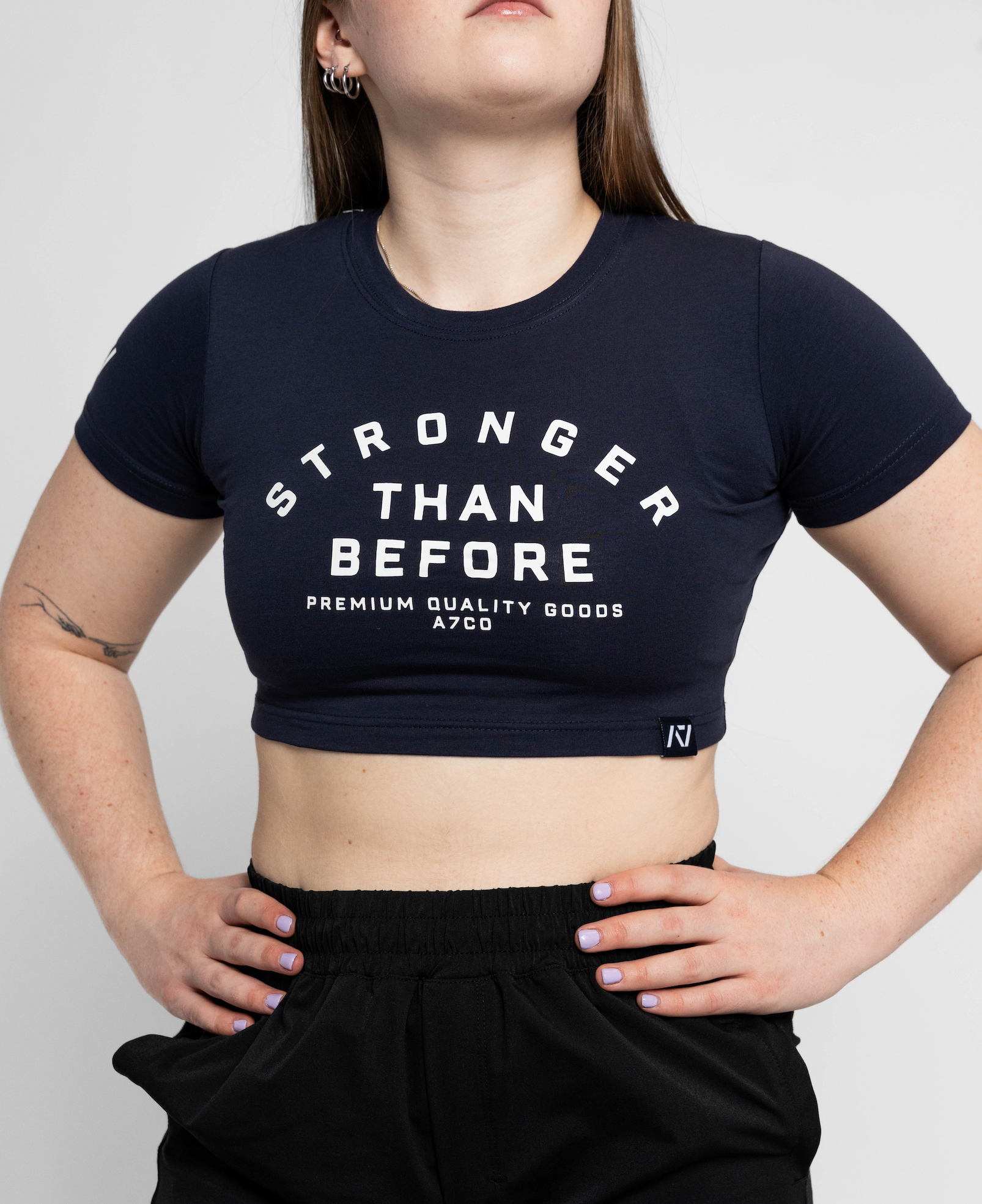 Person wearing a black crop top with 'Stronger Than Before' text on a plain background