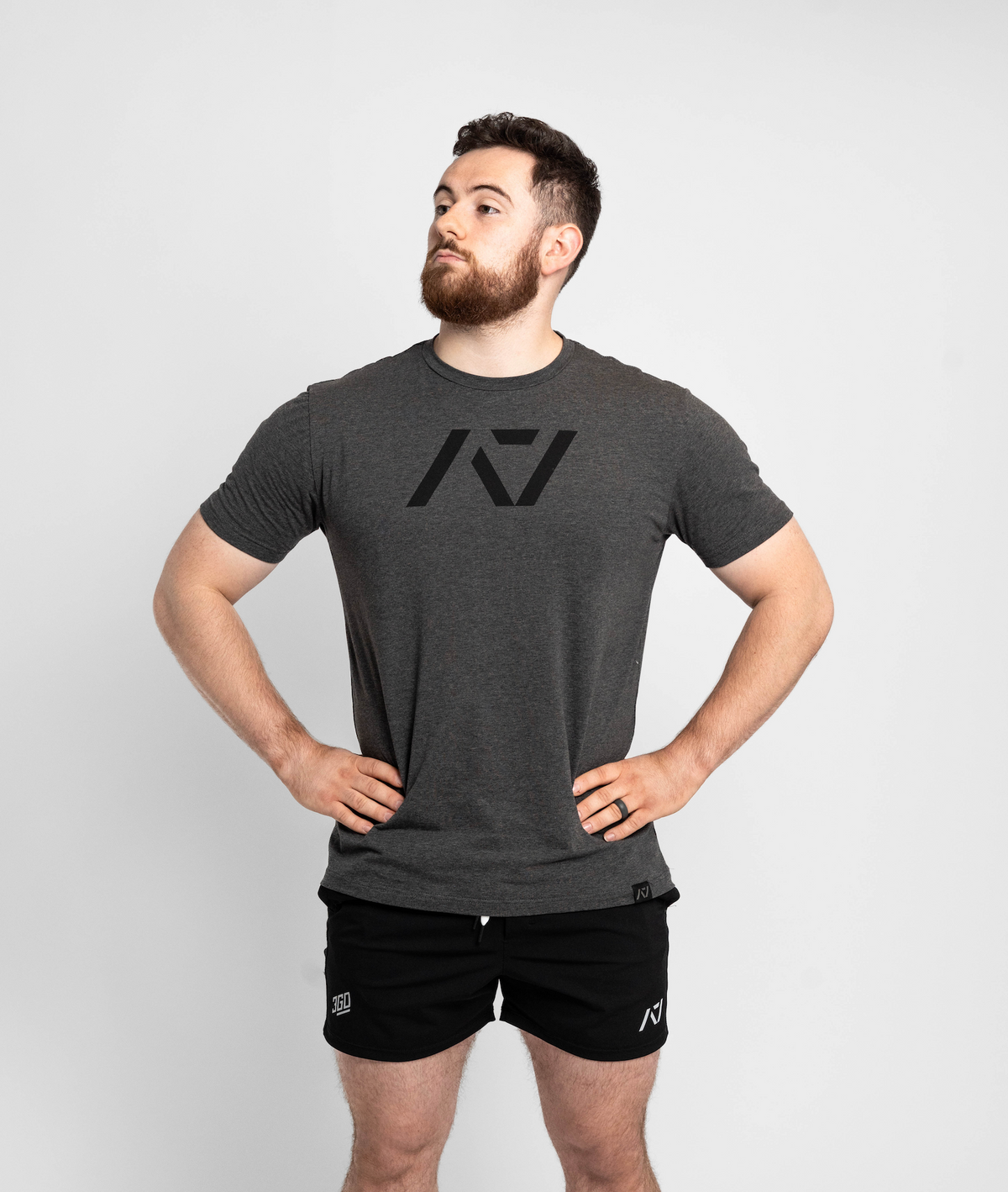 Man wearing a dark gray t-shirt and black shorts with a logo on a light gray background