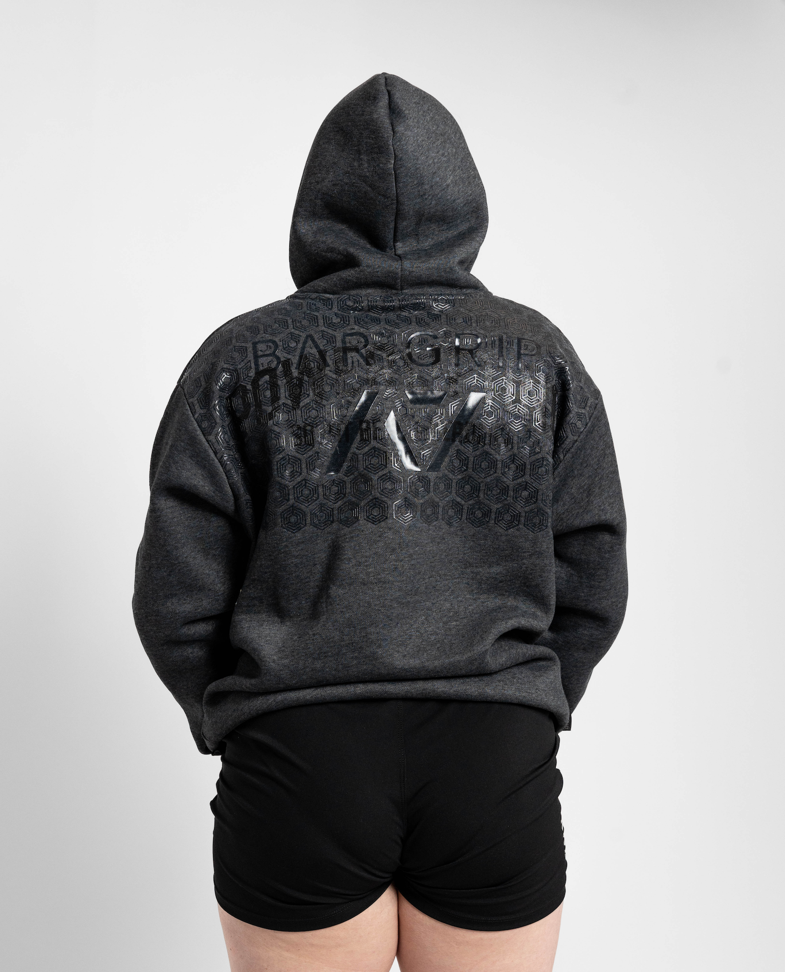 Person wearing a dark gray hoodie with branding on the back against a light gray background