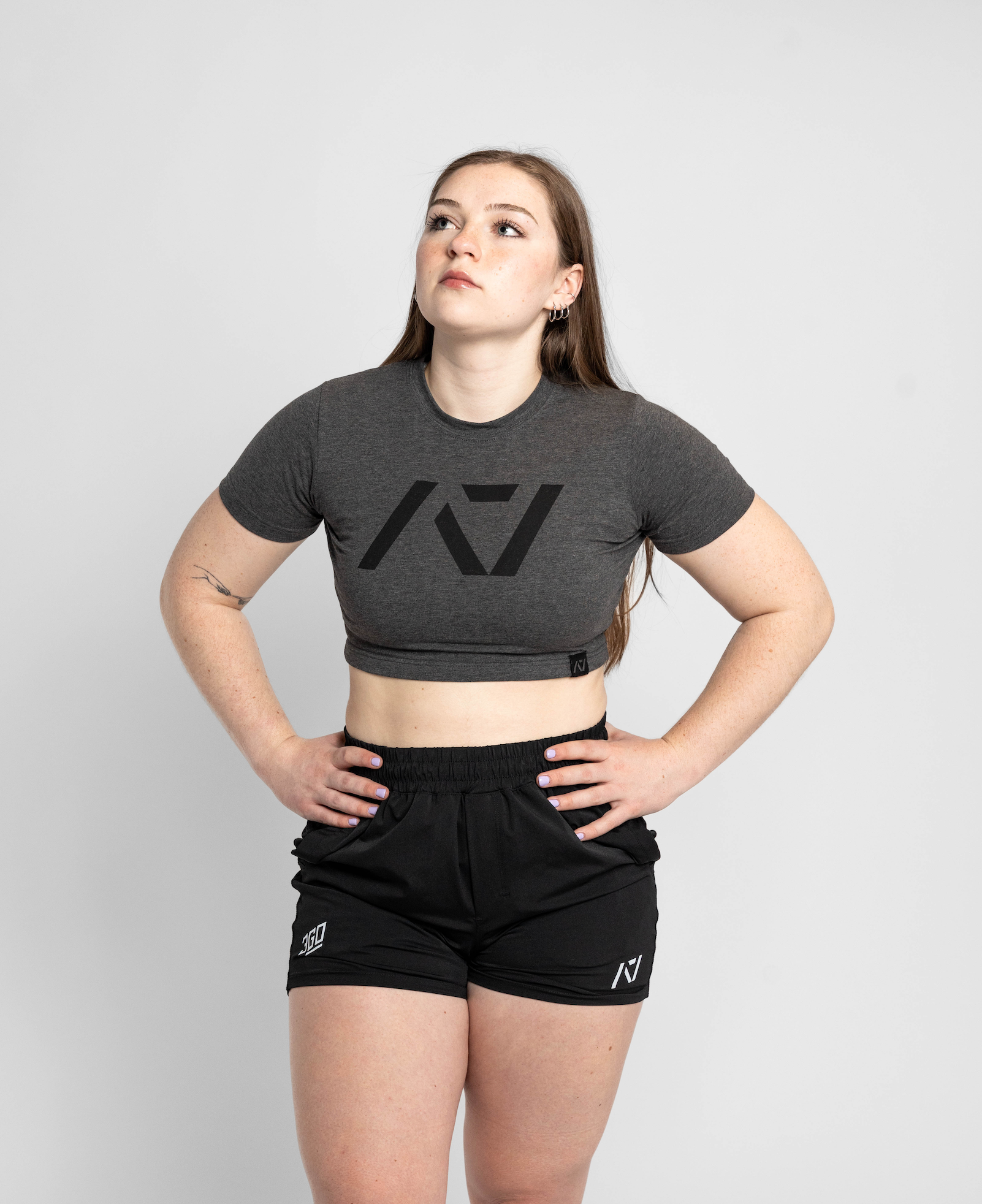 Person wearing a gray crop top with a logo and black shorts on a light gray background