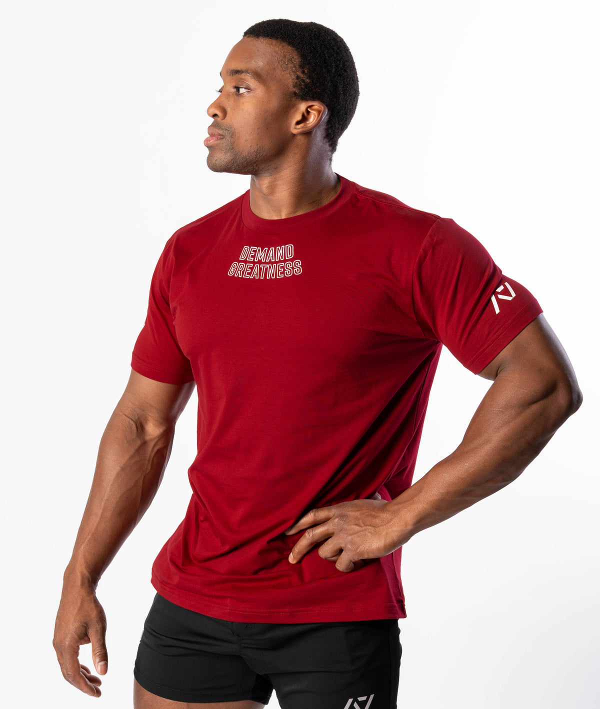 A man wearing a red Demand Greatness True-Fit men's meet shirt with a design on the upper chest and logos on the upper back and sleeves.