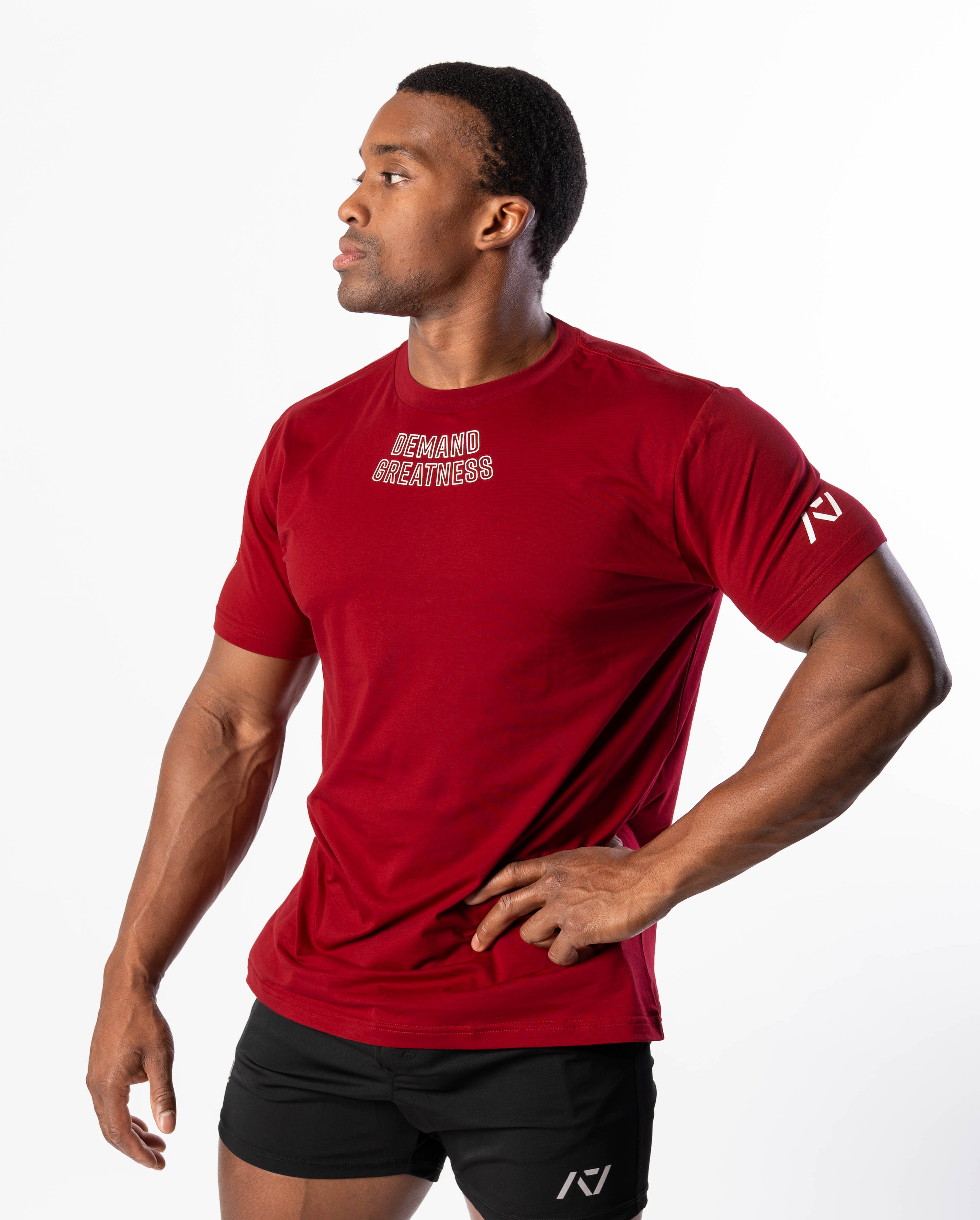 A man wearing a red Demand Greatness True-Fit men's meet shirt with a design on the upper chest and logos on the upper back and sleeves.