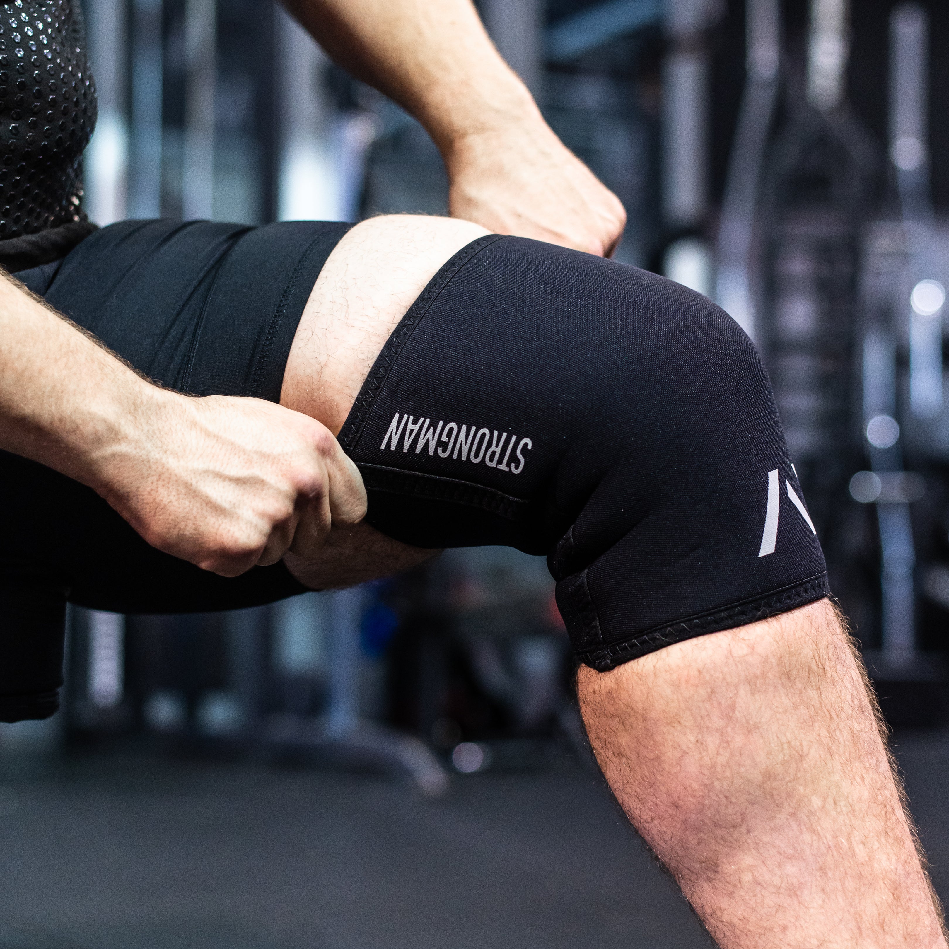 Detailed view of the reflective A7 logo and "Strongman" text on the black knee sleeves, emphasizing branding and design.