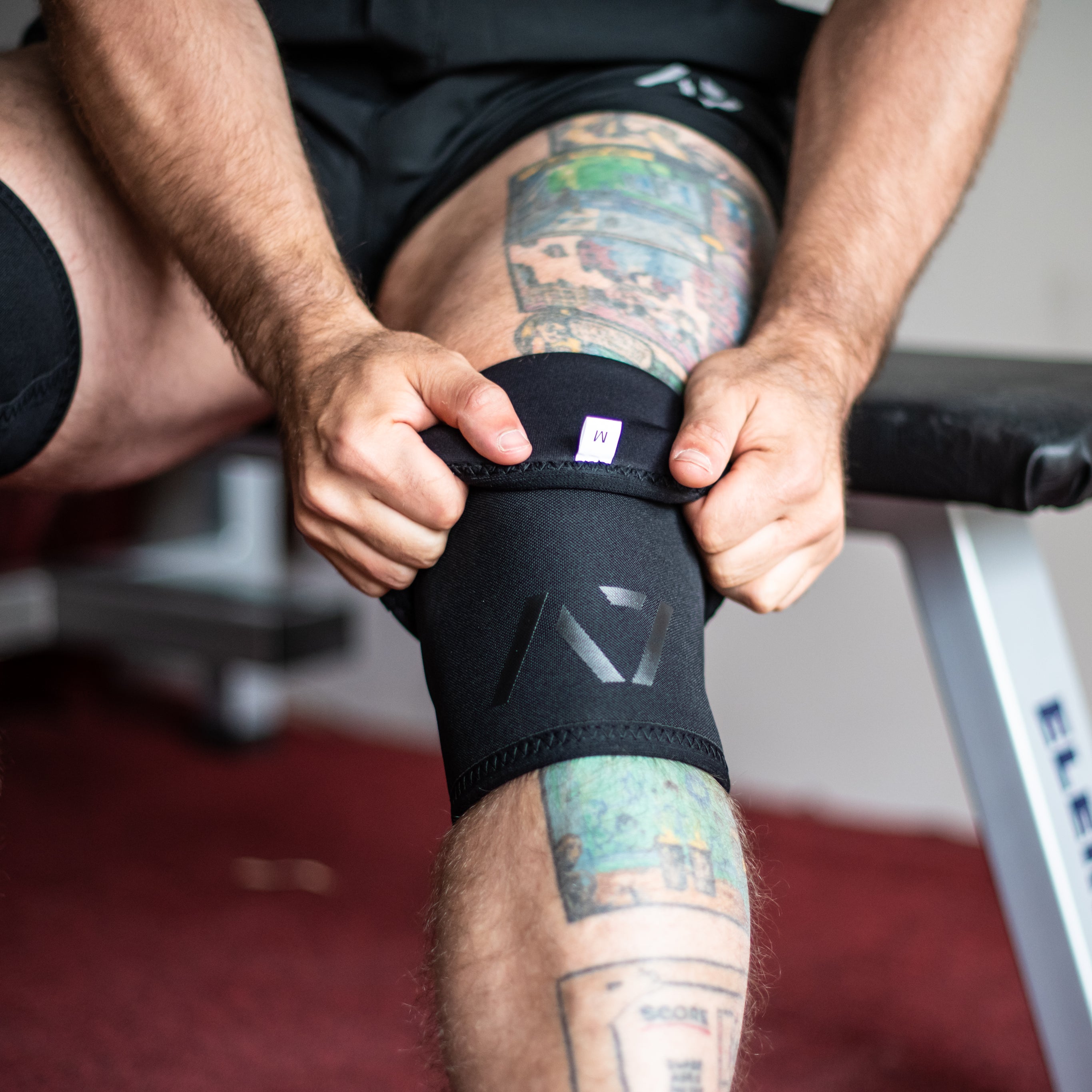 Both A7 Stealth Stiff CONE Knee Sleeves on Lifters knees displaying the pair of sleeves and putting them on knees.