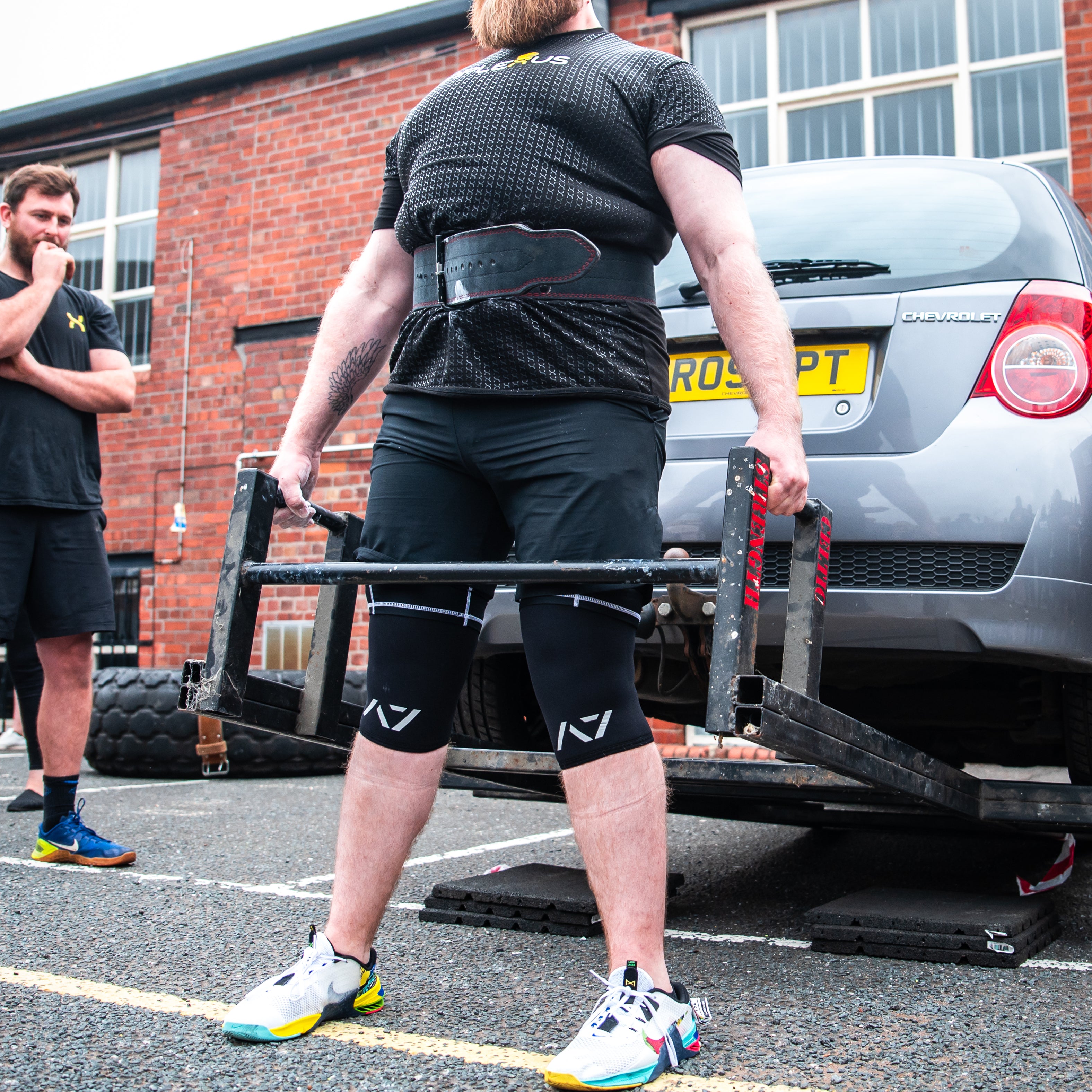 Athlete performing a car deadlift wearing A7 Strongman Knee Sleeves – 9mm – Black/Reflective, showcasing enhanced knee support during strongman training.