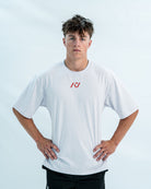 Male wearing a white over-fit shirt with a red logo on a light gray background