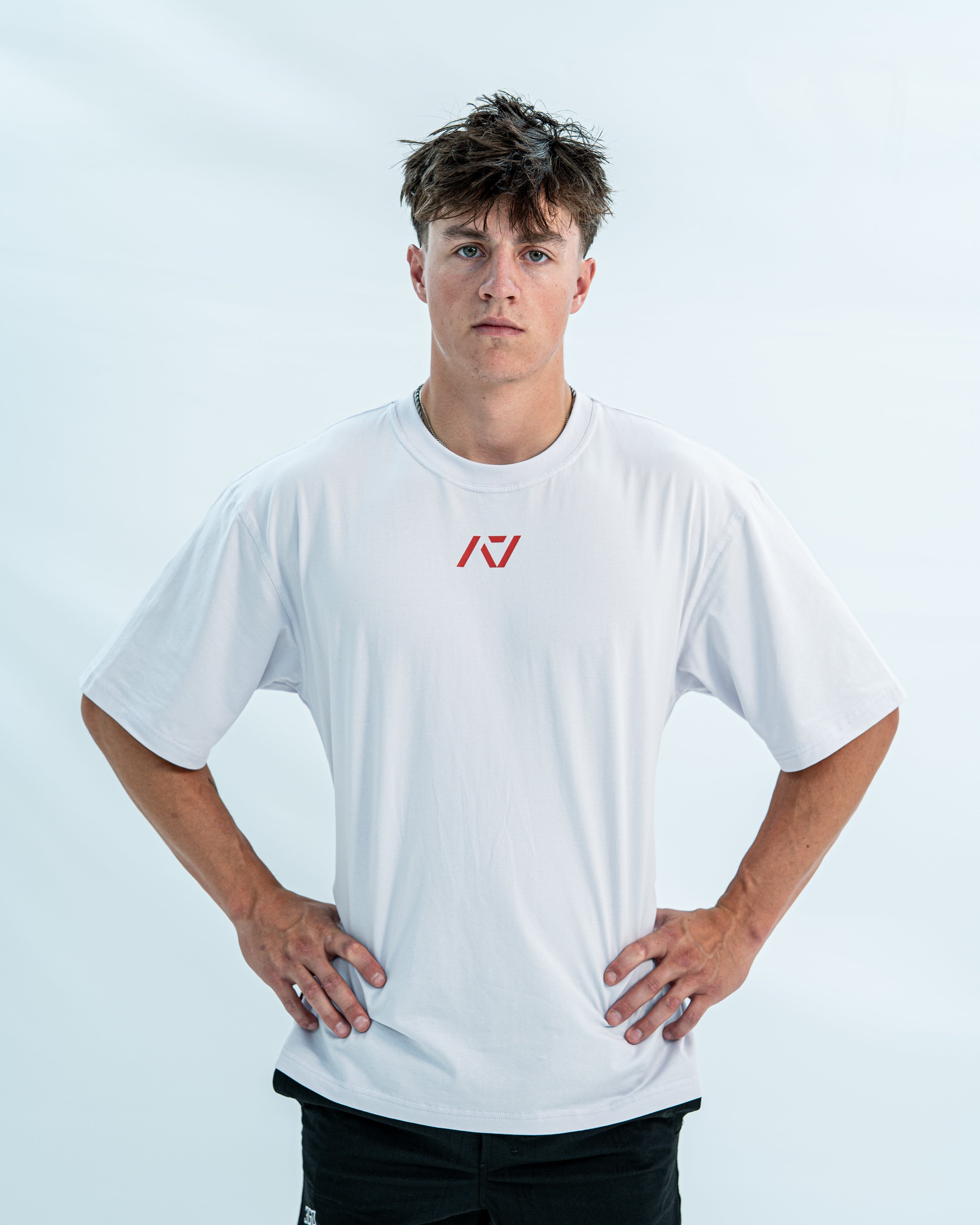 Male wearing a white over-fit shirt with a red logo on a light gray background