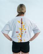 Female wearing a white over-fit shirt with a design on the back against a light gray background