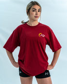 Female wearing a red over-fit shirt with a logo on a light gray background