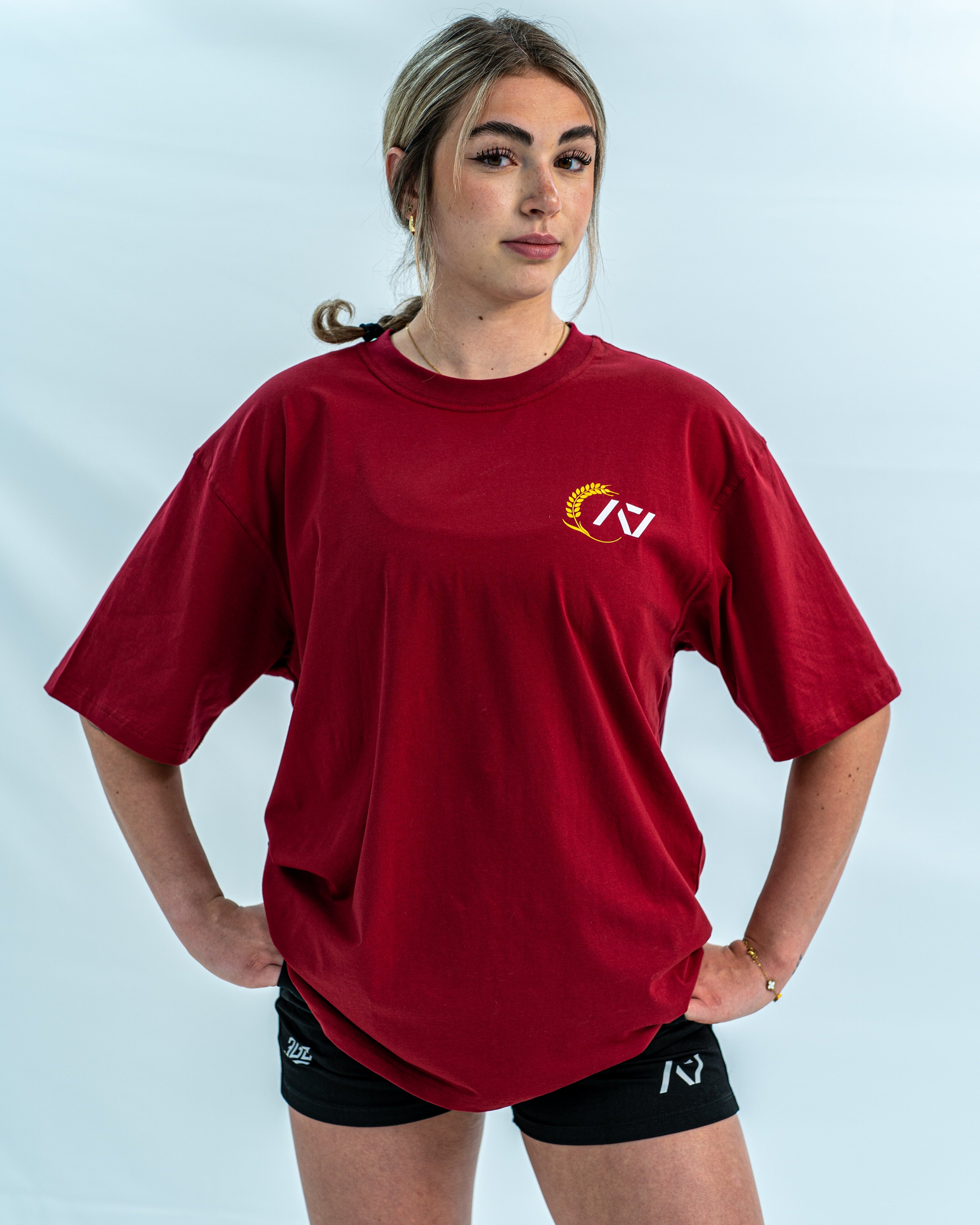 Female wearing a red over-fit shirt with a logo on a light gray background