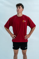 Male wearing a red over-fit unisex shirt with a logo on a light gray background