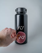 Black water bottle with sticker getting placed onto the bottle on a gray background