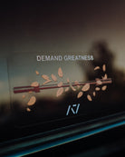 Decorative decal with 'DEMAND GREATNESS' text and an barbell design on a car window.