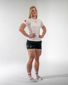 Woman wearing a white athletic shirt with red accents and black shorts on a white background
