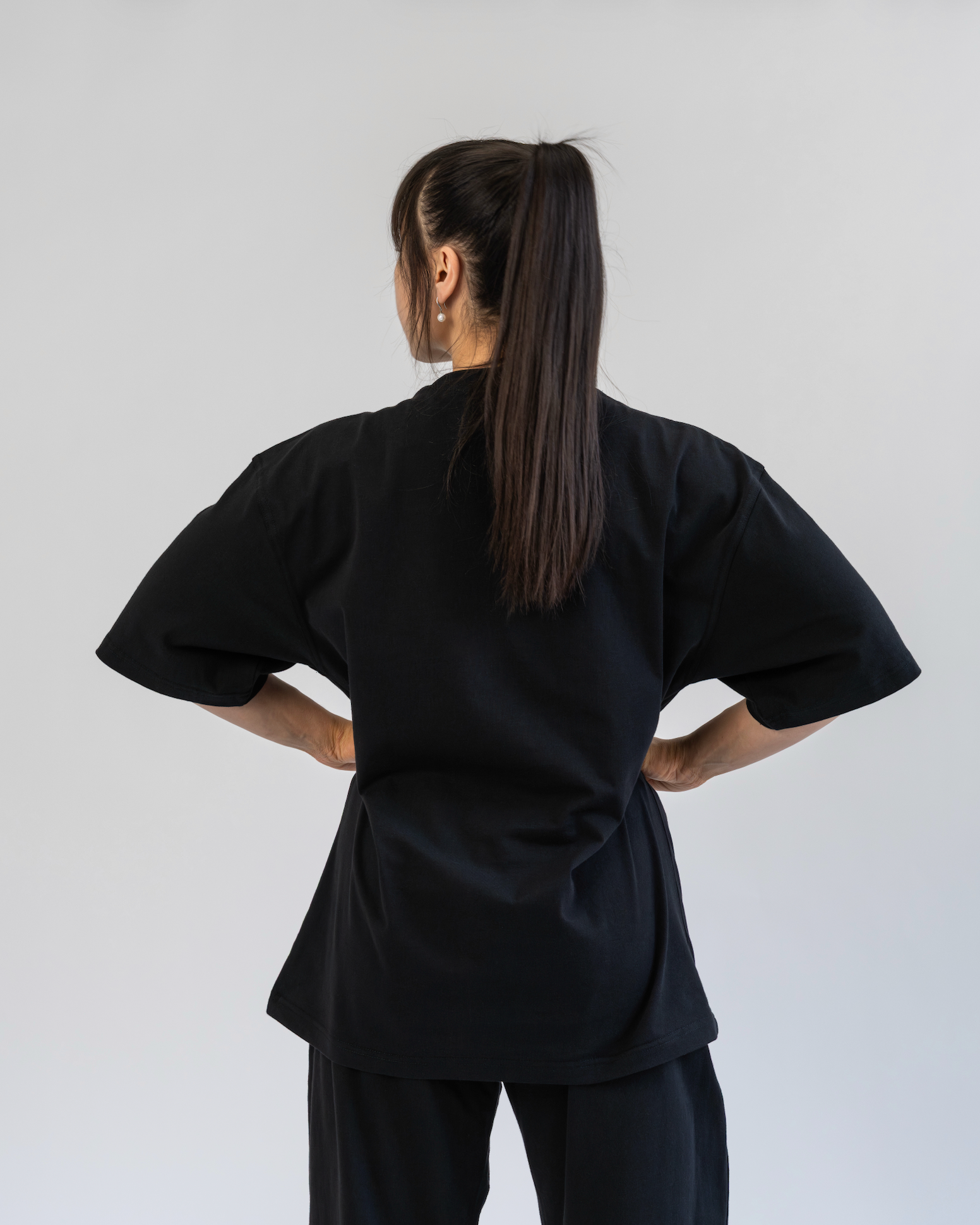 Person wearing a black outfit with wide sleeves and pants on a plain background