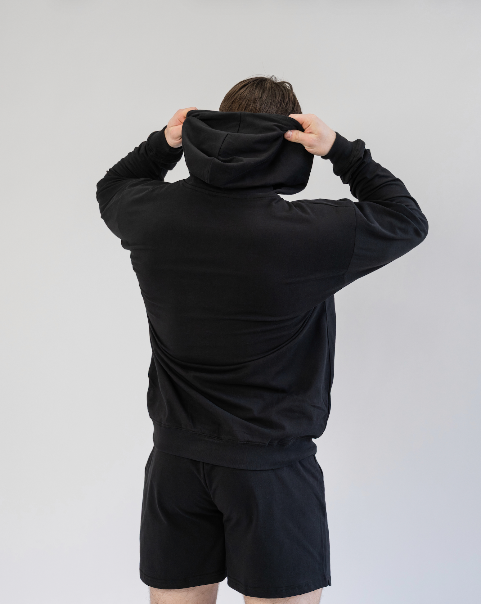 Person wearing a black hoodie and shorts set against a plain background