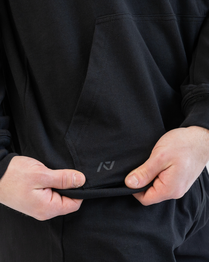 Person wearing a black hoodie with a logo on the chest pocket against a light gray background
