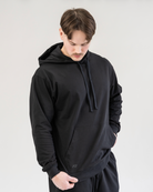 Man wearing a black hoodie and pants against a plain background