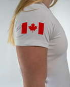 Person wearing a white t-shirt with a red maple leaf design on a plain background