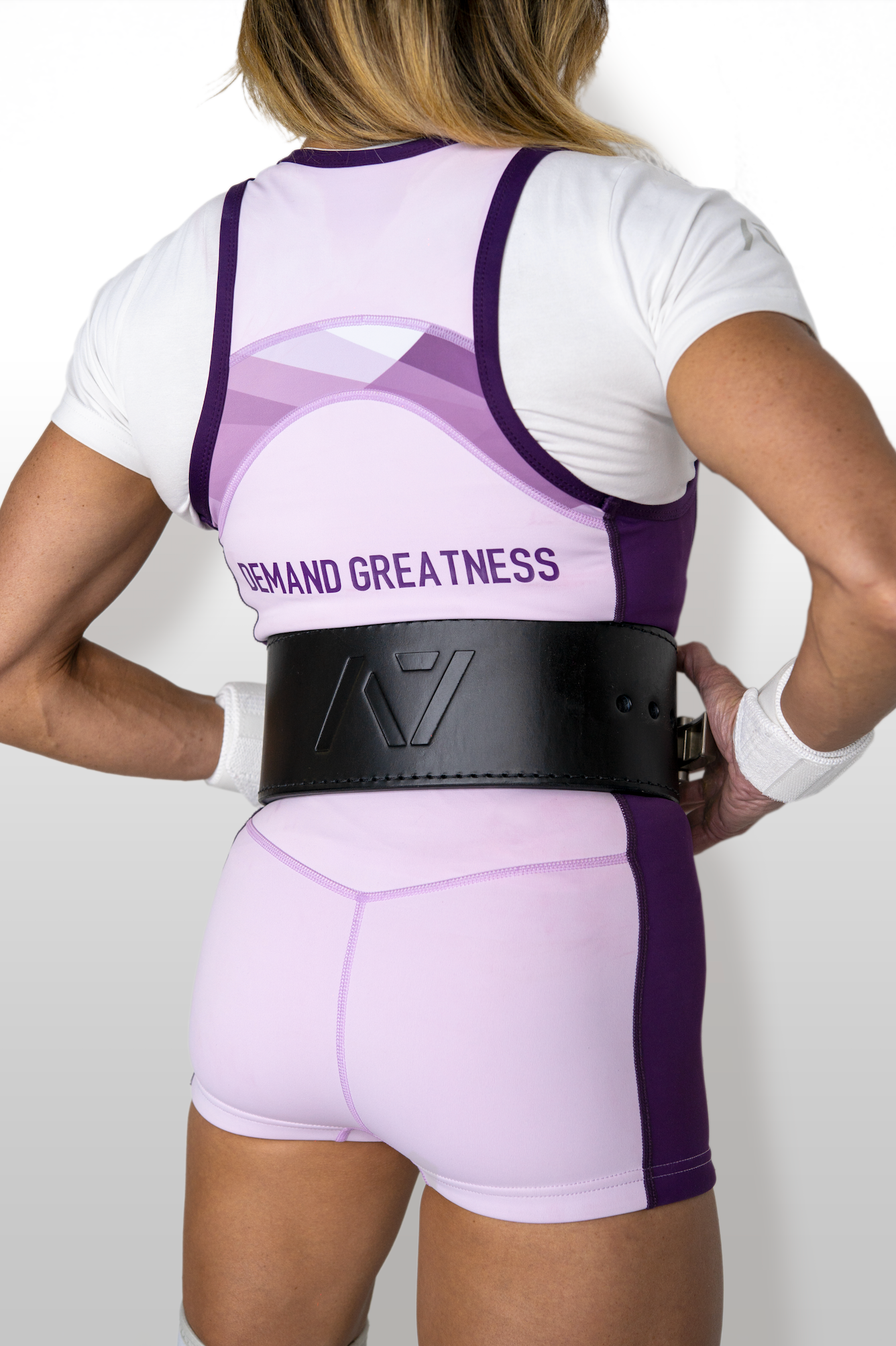 Person wearing a white and purple IPF approved powerlifting singlet with a black belt on a plain background